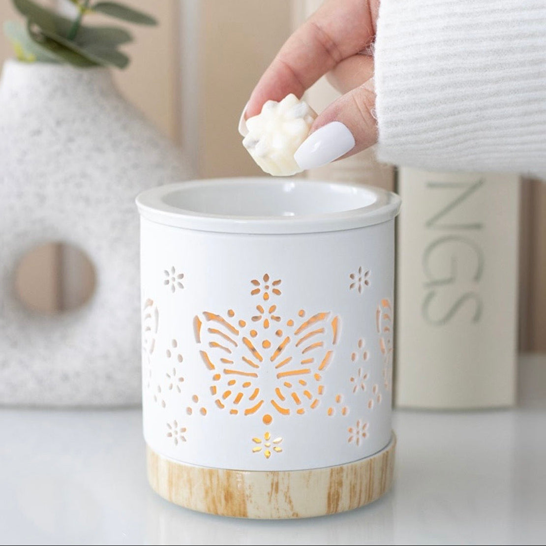 White wax warmer with butterfly design on a wooden base, used to melt wax for diffusers.
